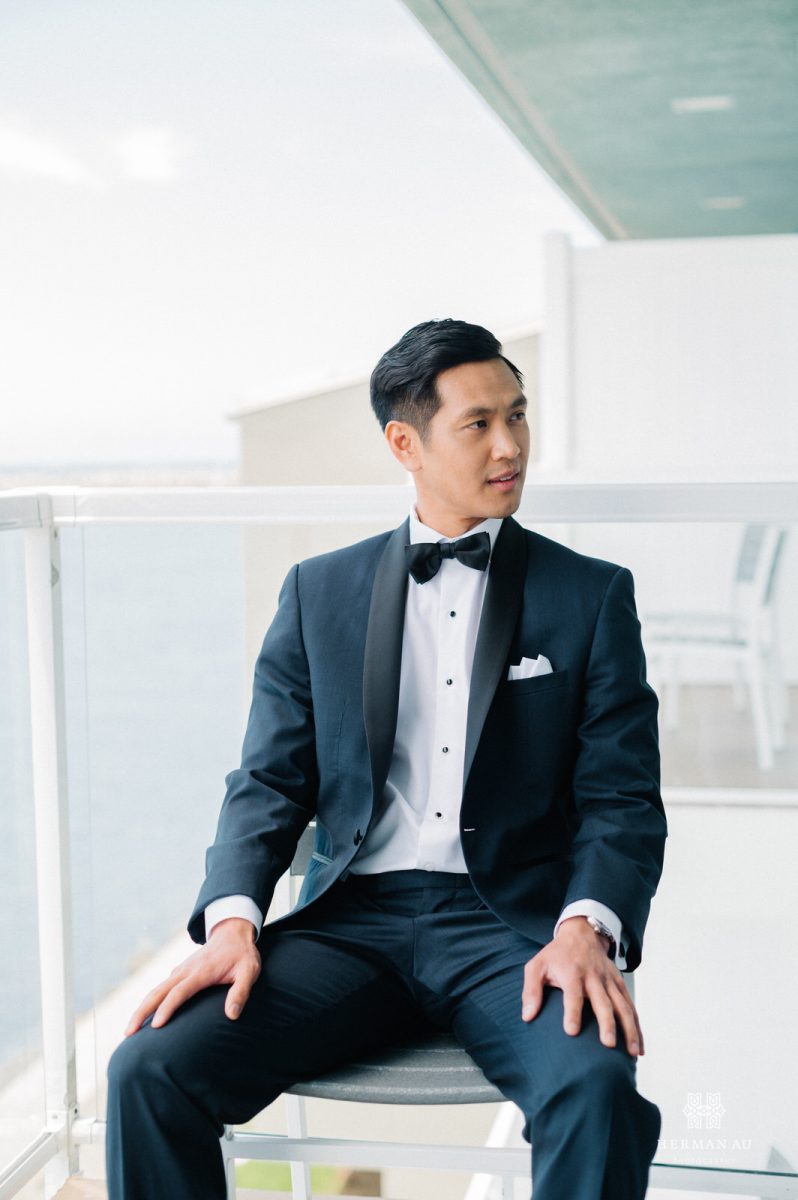 Groom wearing a tux sitting in a chair and looking off to the side