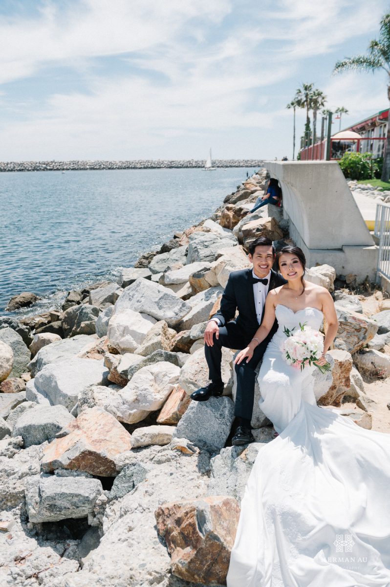Bride and groom sitting on the rocks with the Redondo Beach Marina in the background 